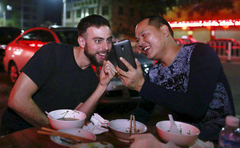 BuzzFeed writer Matt Stopera (L) of the U.S. and "Brother Orange" Li Hongjun of China smile as they look at a mobile phone at a restaurant in Meizhou, Guangdong province March 18, 2015. Stopera's iPhone was lost in New York last year and it ended up with its new owner in south China, whose selfie photos in front of mandarin orange trees showed up in January on Stopera's photo stream. Their story went viral after Stopera posted those selfie photos on the Internet, and Chinese netizens helped him track down "Brother Orange". Stopera arrived in Guangdong on Tuesday night and they will tour the city where "Brother Orange" grew up, according to local media. REUTERS/Stringer