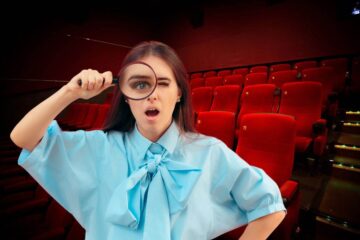ragazza con lente d'ingrandimento e dietro una sala cinematografica