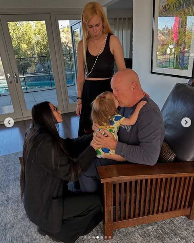 Bruce Willis seduto in poltrona con un bambino sulle gambe, Demi Moore di fronte e la figlia di Bruce accanto a lui